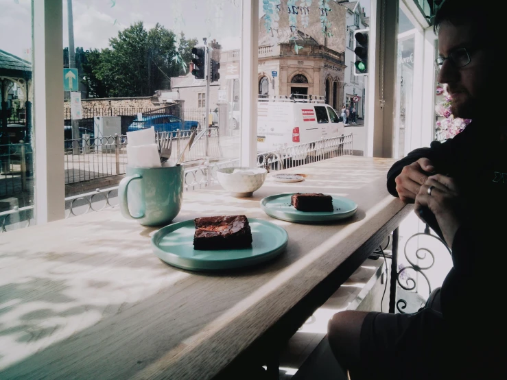 a man sitting at a window with a plate of cake