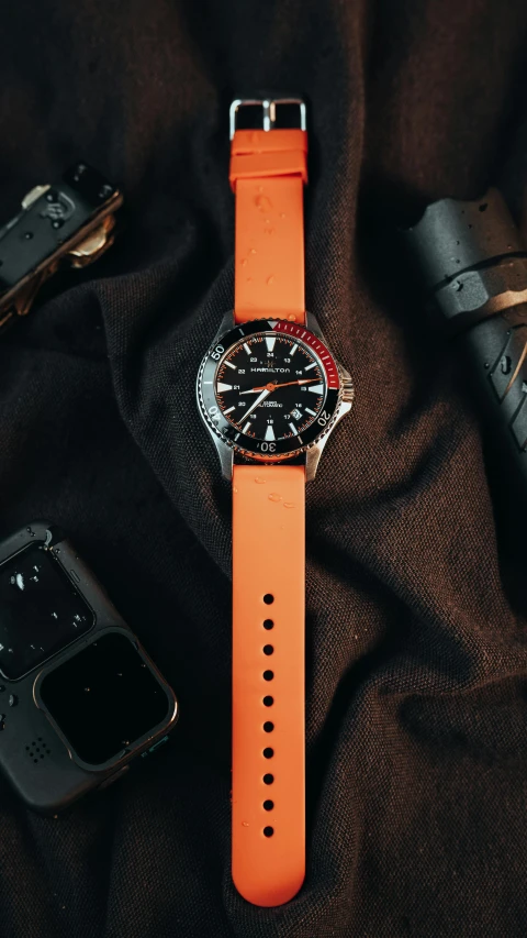 an orange watch sitting on top of a table with cellphones