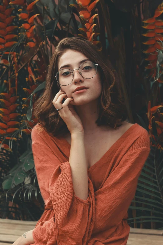 a woman with glasses and a red sweater sits in a chair near flowers