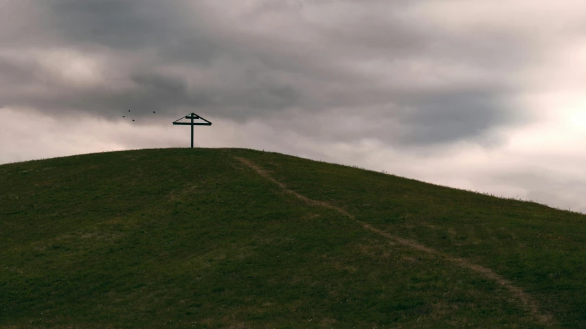 a cross on a hill under cloudy skies