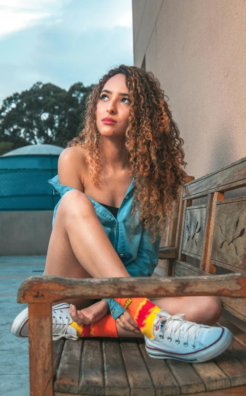 an attractive young woman with curly hair sitting on a bench