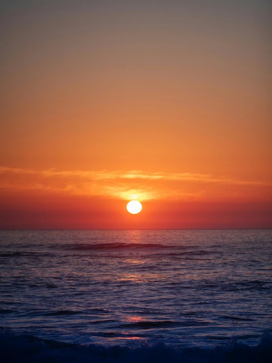 a bright sunset over the ocean as a sail boat glides under