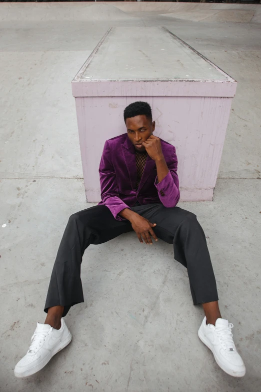 a man in purple sits on the ground near a trunk