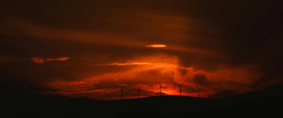 a red and orange sky with clouds, with wind mills