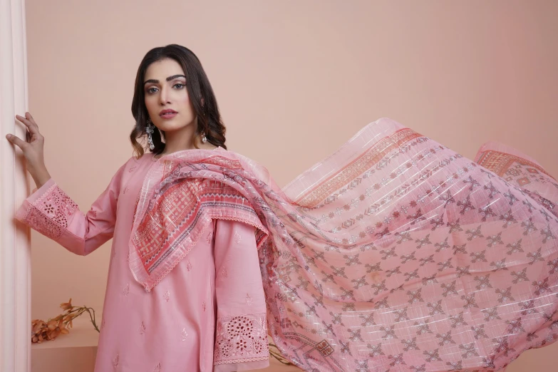 a woman standing in front of a pink wall holding a piece of lace