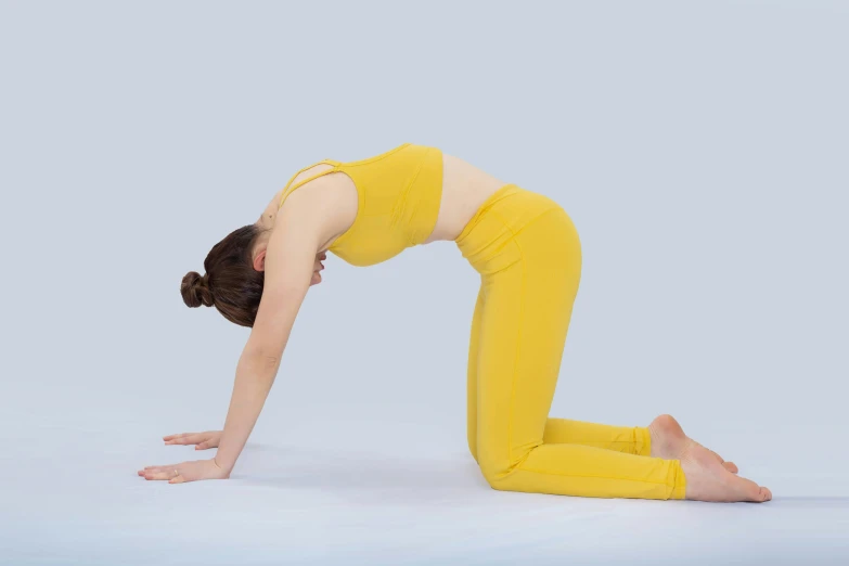 woman in a yellow yoga outfit does a stand - on handstand pose