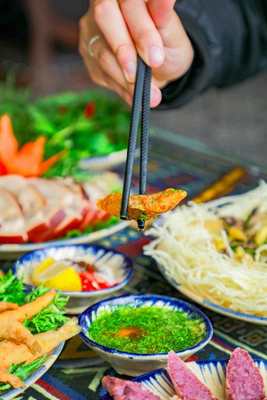 a person is holding chopsticks out towards food on the table