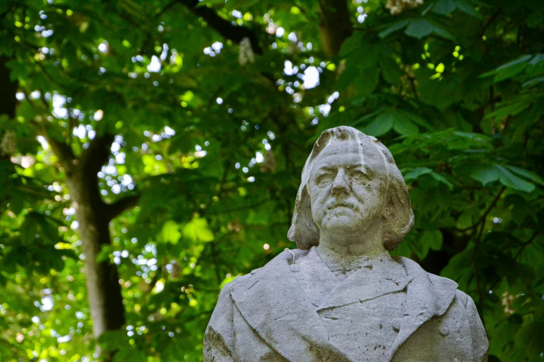 there is a stone statue of a man in a cloak with trees in the background