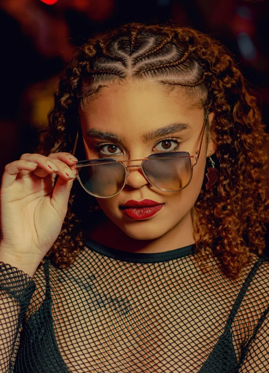 woman in fishnet shirt holding sunglasses and looking at camera