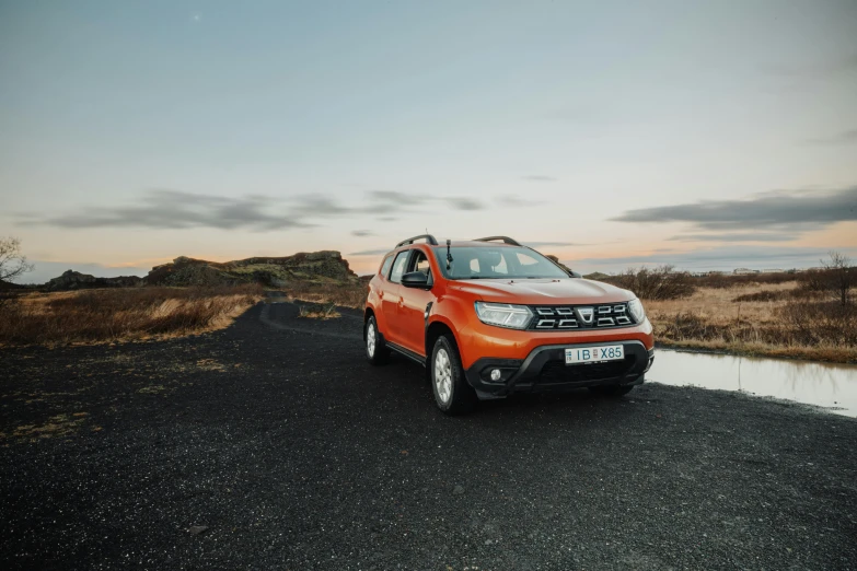 an orange colored car sitting by the water