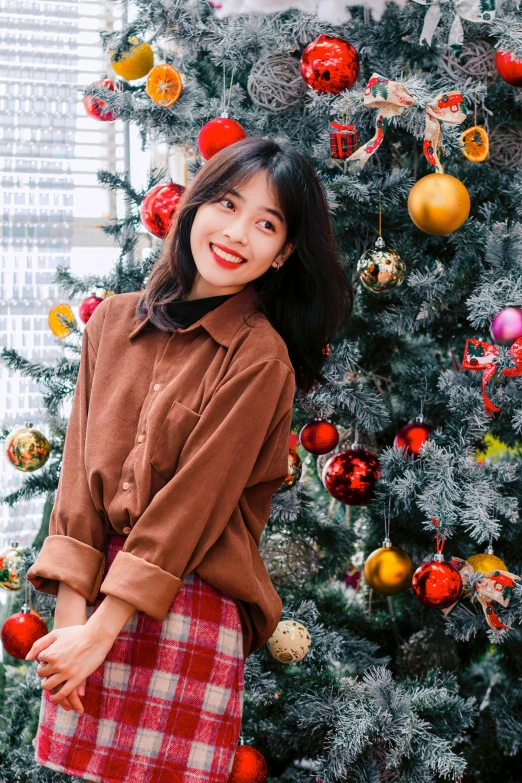 a girl is standing by the christmas tree and smiling