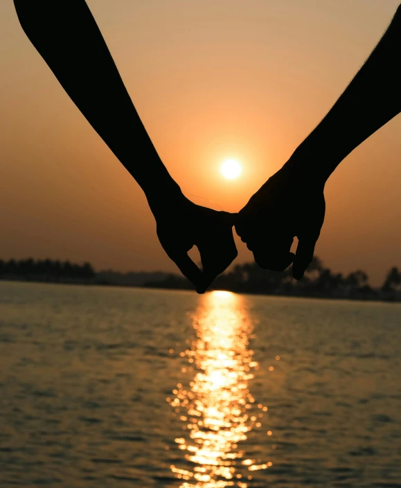 two persons holding hands by a body of water