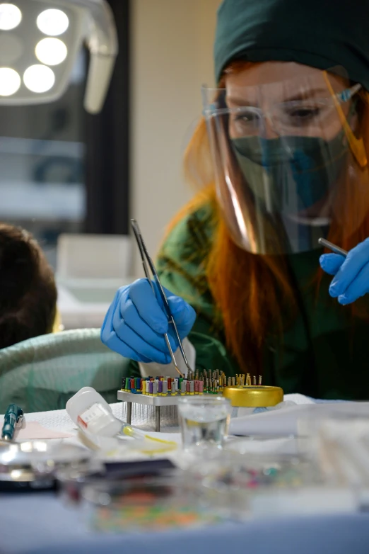 a woman wearing blue gloves and safety equipment holding paint brushes