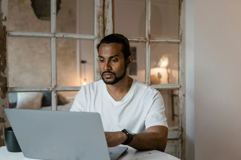 a man working on his laptop computer while sitting at a table