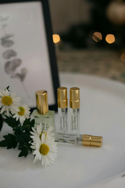 three small clear bottles, one on a table and some daisies with the contents beside them