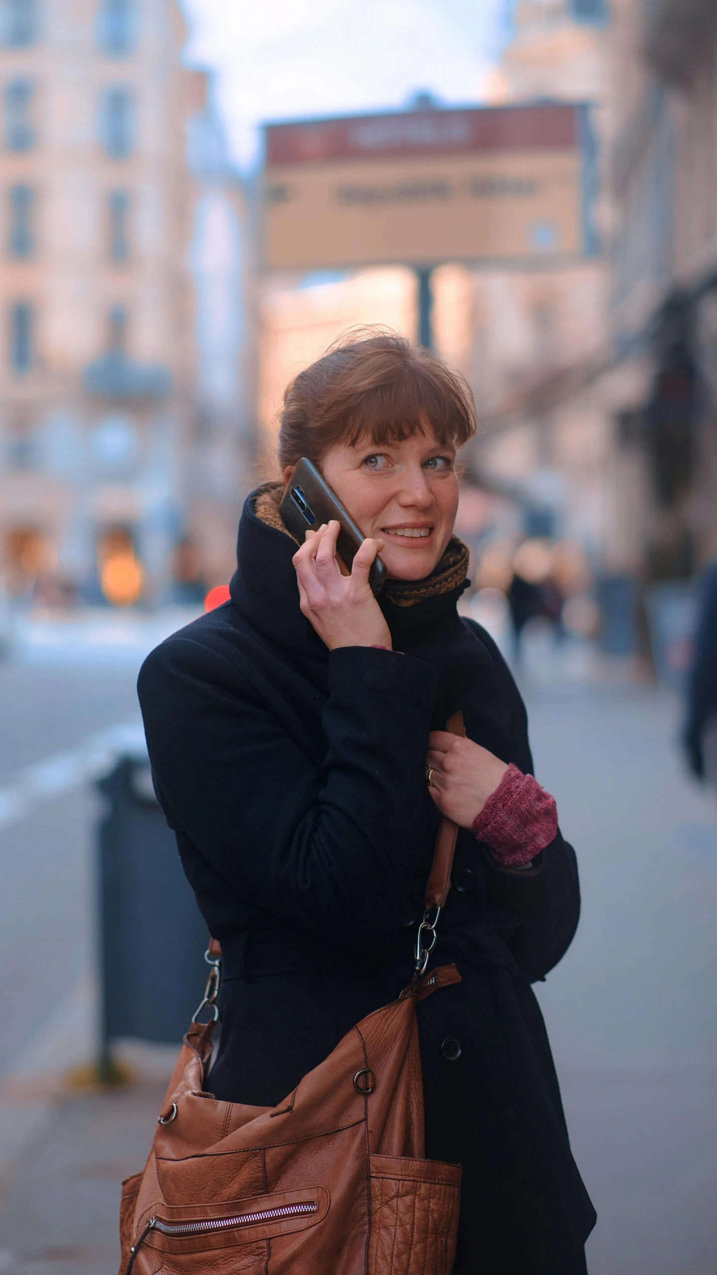 a woman in a black jacket and scarf talks on a cell phone