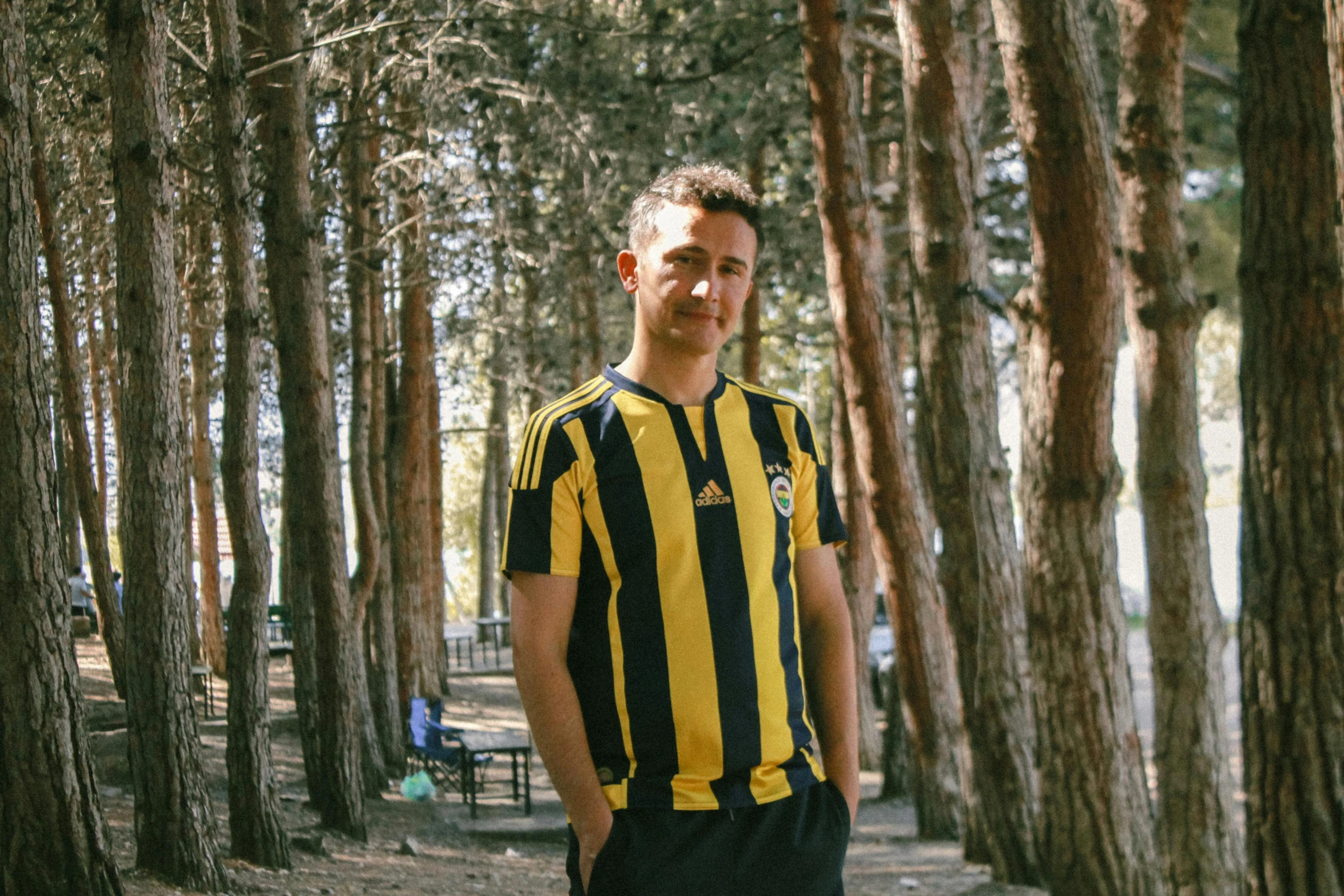 a young man wearing a black and yellow striped shirt standing in the woods