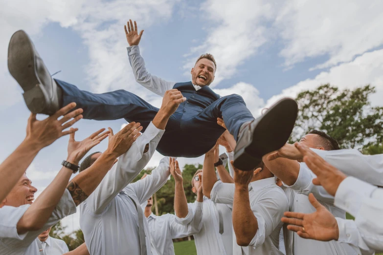 a man in white shorts and a blue jacket balances his head high in the air while others surround him