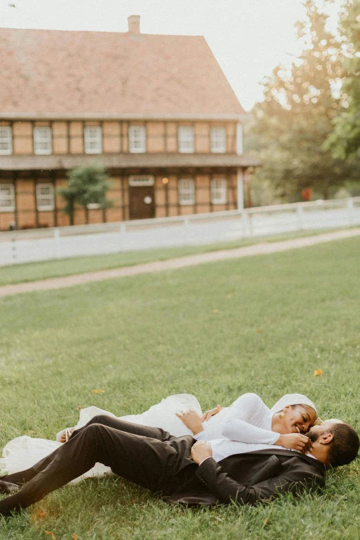 a young couple laying on a green lawn outside a house