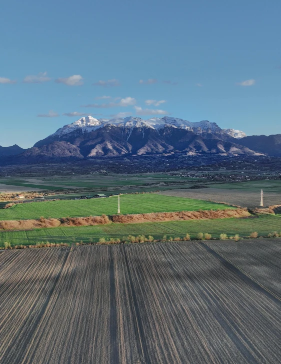 a farm field with snow covered mountains behind it