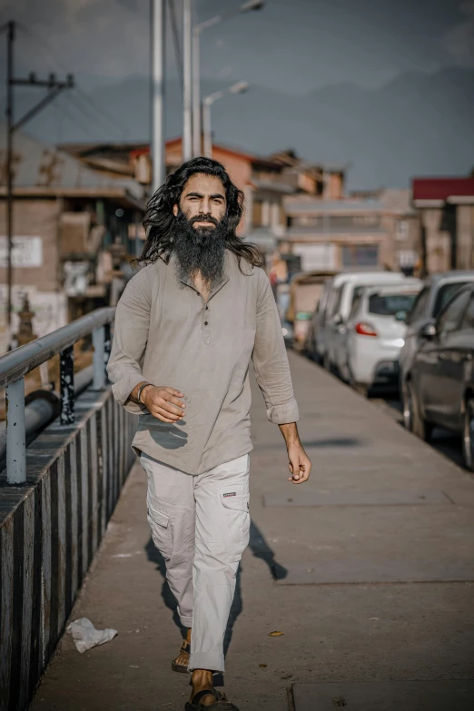 a man with long hair and beard walks along the sidewalk