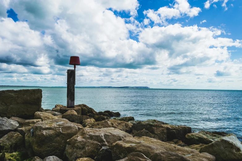 a red sign on a rock wall with the ocean and sky in the background