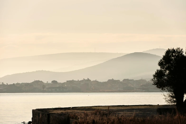 a bench sitting next to the ocean with a small town and mountains in the background