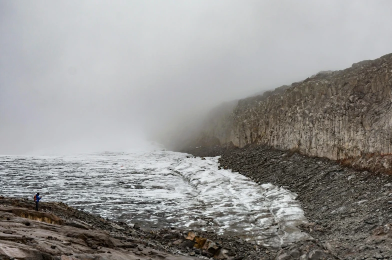 a person is walking along the shoreline in front of mountains