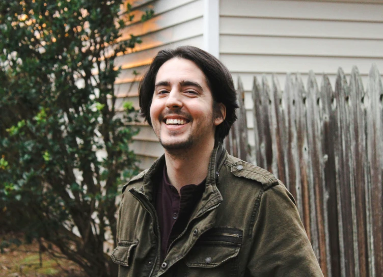 a smiling man standing in front of a house