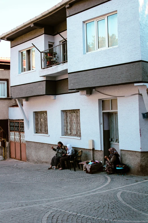 three men sitting outside in front of a white building