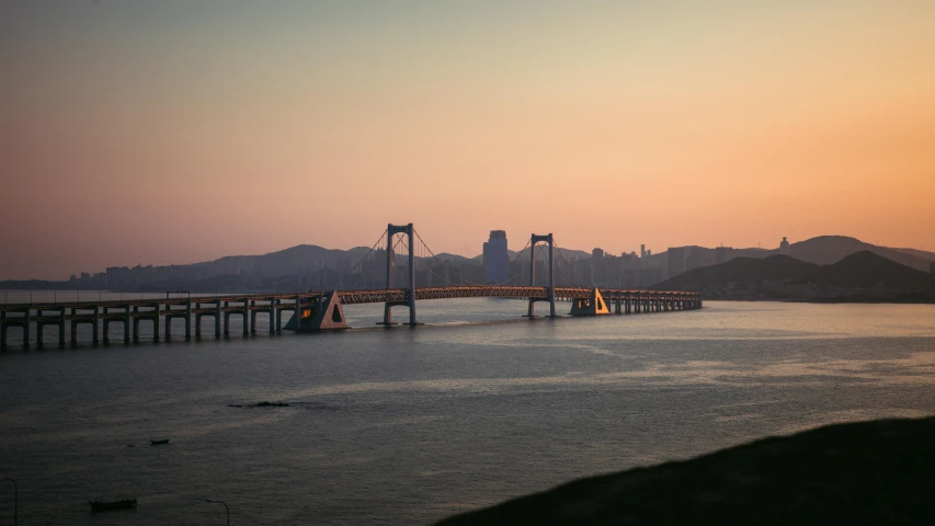 the bridge is going into a city with mountains in the background