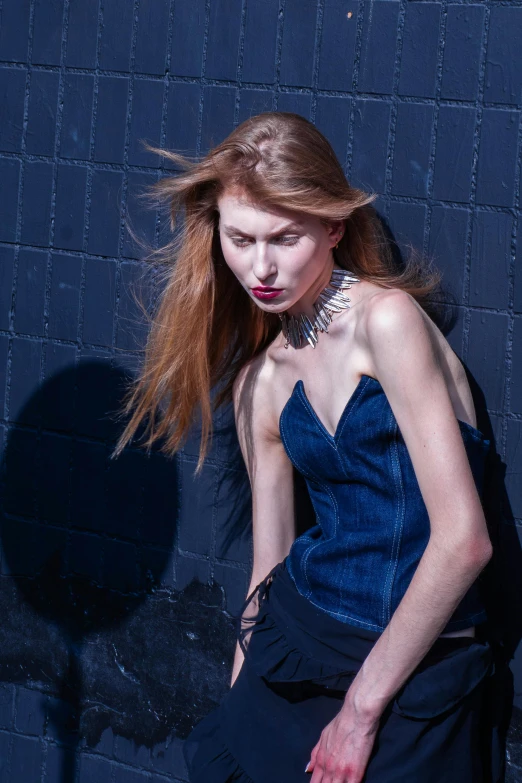 a woman wearing a blue dress leaning against a black wall