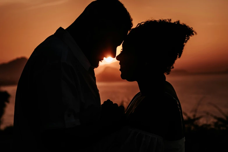 a couple standing next to each other on a hill at dusk