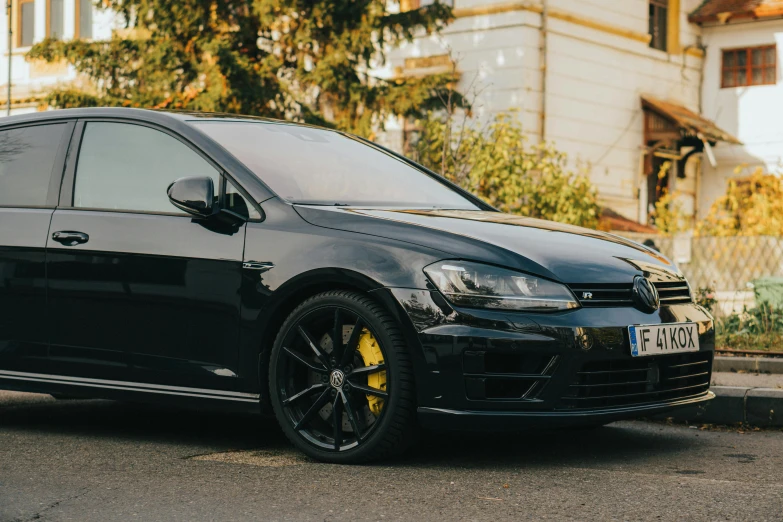 black vw golf with yellow wheels is sitting on the street