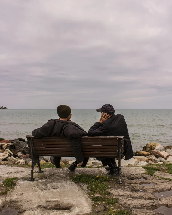 two people sitting on a bench near the water