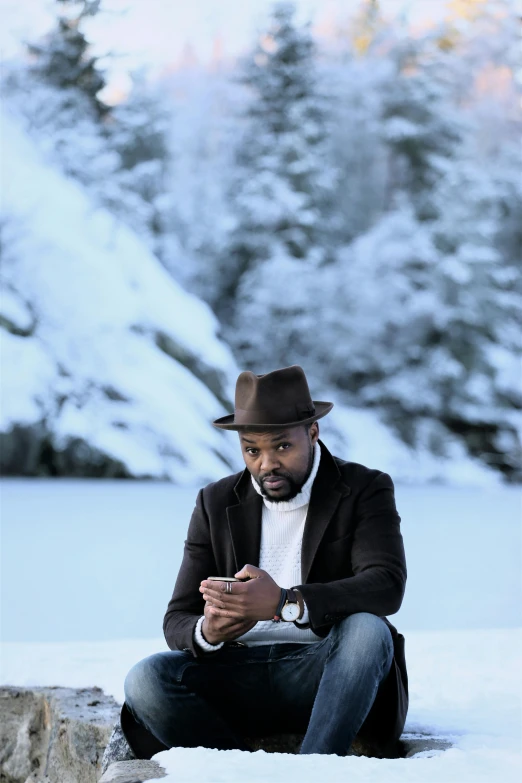 a man is sitting in the snow and looking at his phone