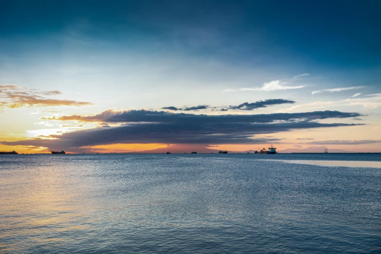 the clouds glow orange as the sun sets over boats in the water