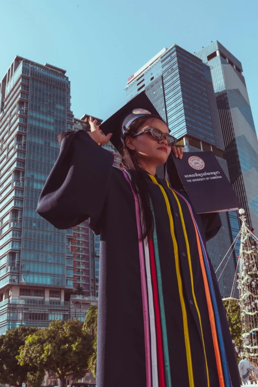 a woman with a graduation gown and a cap stands next to tall buildings