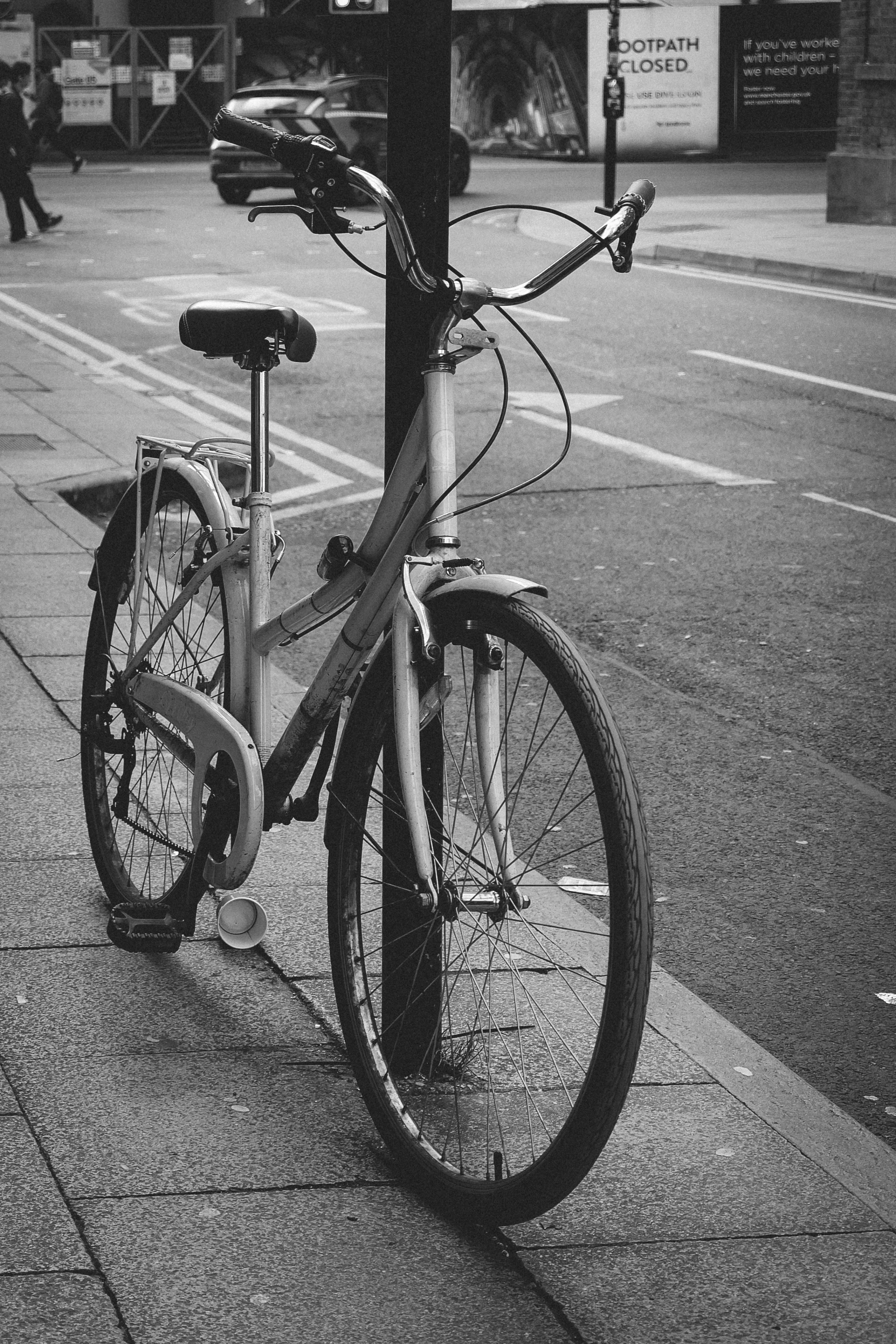 an old bike locked on the pole of a busy city street