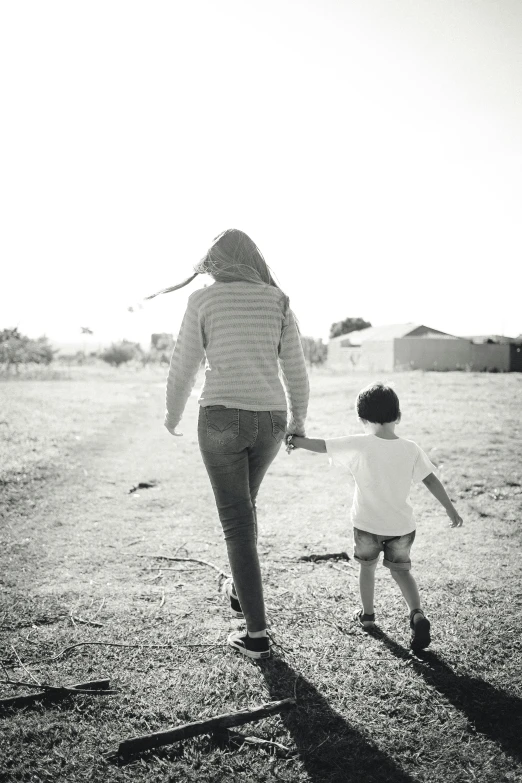 the woman holds her hand out to the child, as they walk through the field