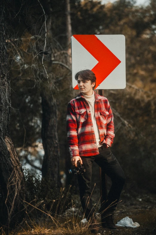 a man stands in a wooded area with a red sign