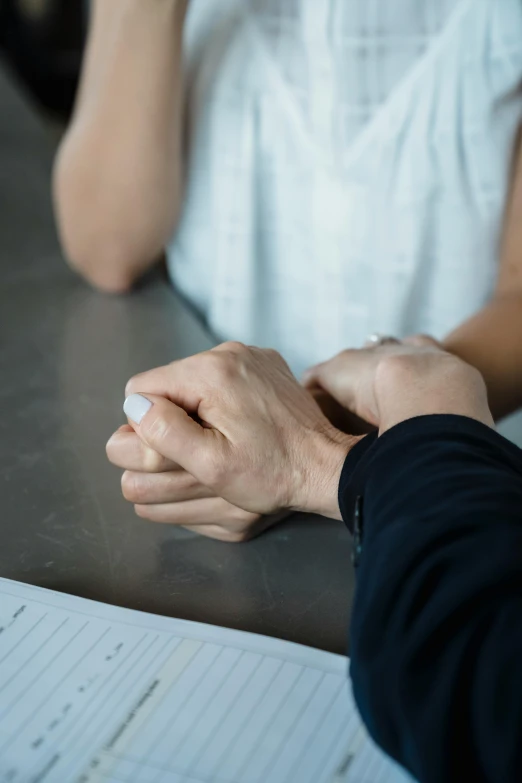 two people are sitting at a table with their hands clasped together