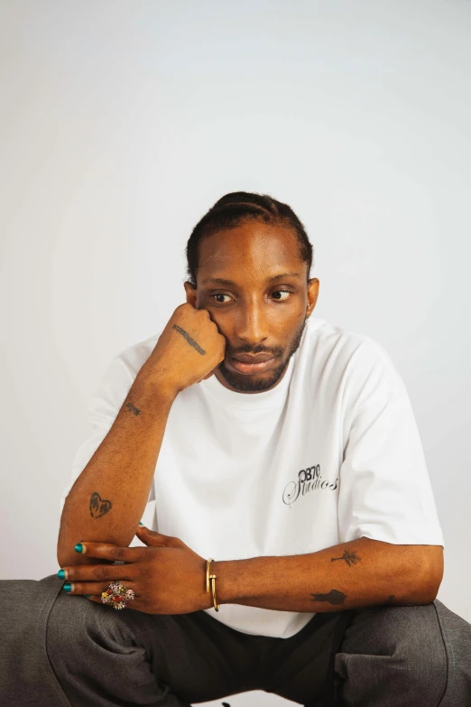 a man with tattoos sits in front of a white wall