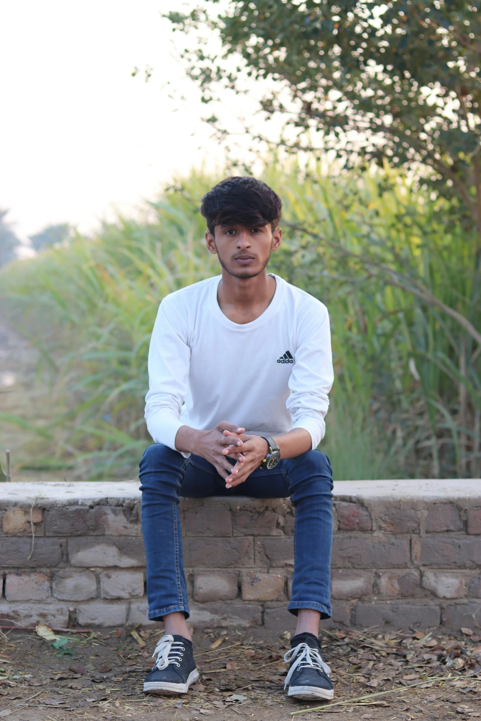 a young man sitting on a brick wall in his sneakers