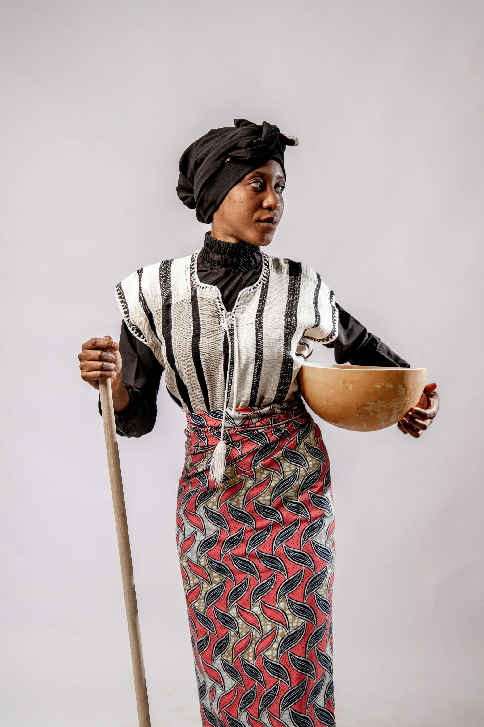 a woman holding a wooden bowl and a stick