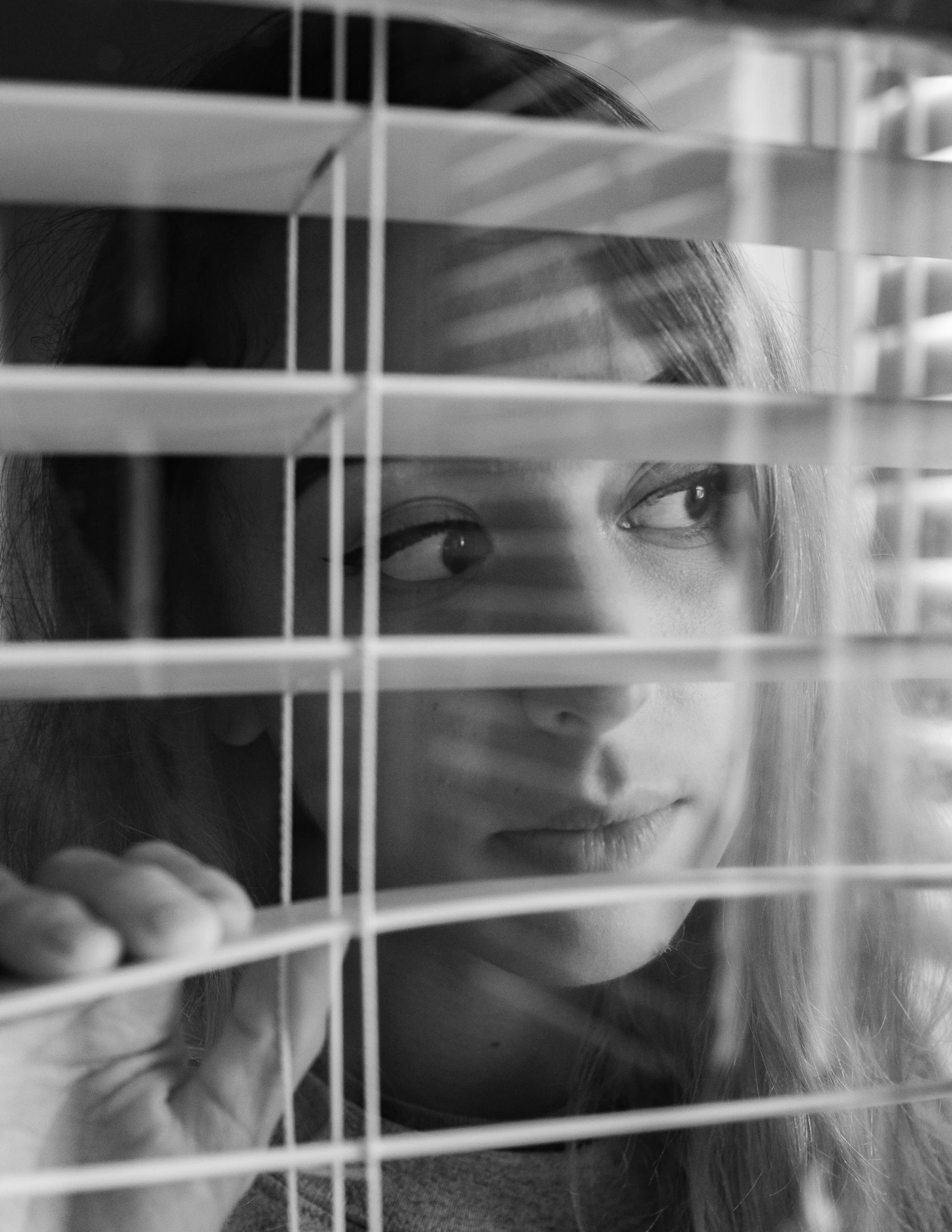 two girls looking out the window covered in blinds