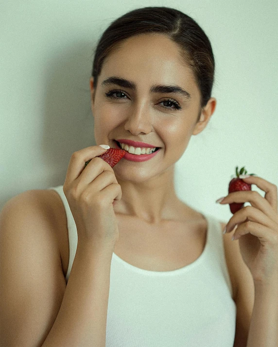 a girl is holding a strawberries for her face