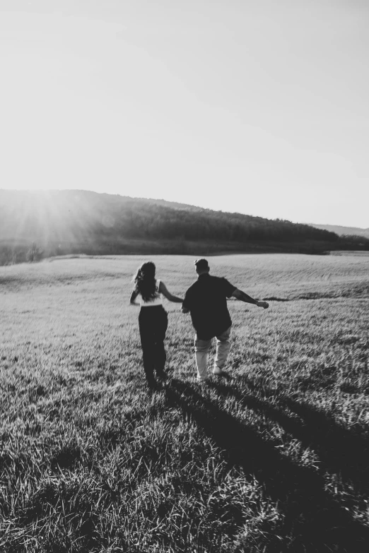 couple walking through grassy field with sun shining down