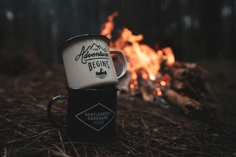 a coffee mug sitting next to an open fire in the woods