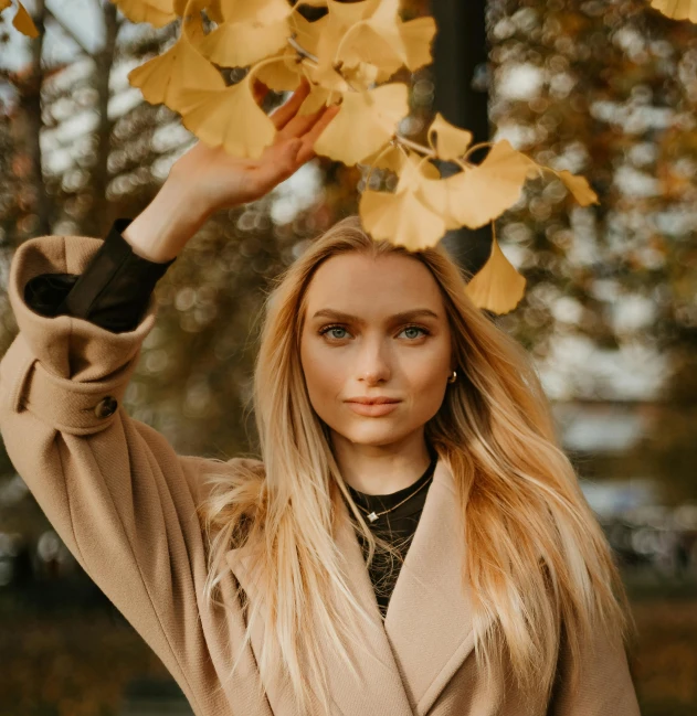 the young blonde woman is posing under the leafy tree